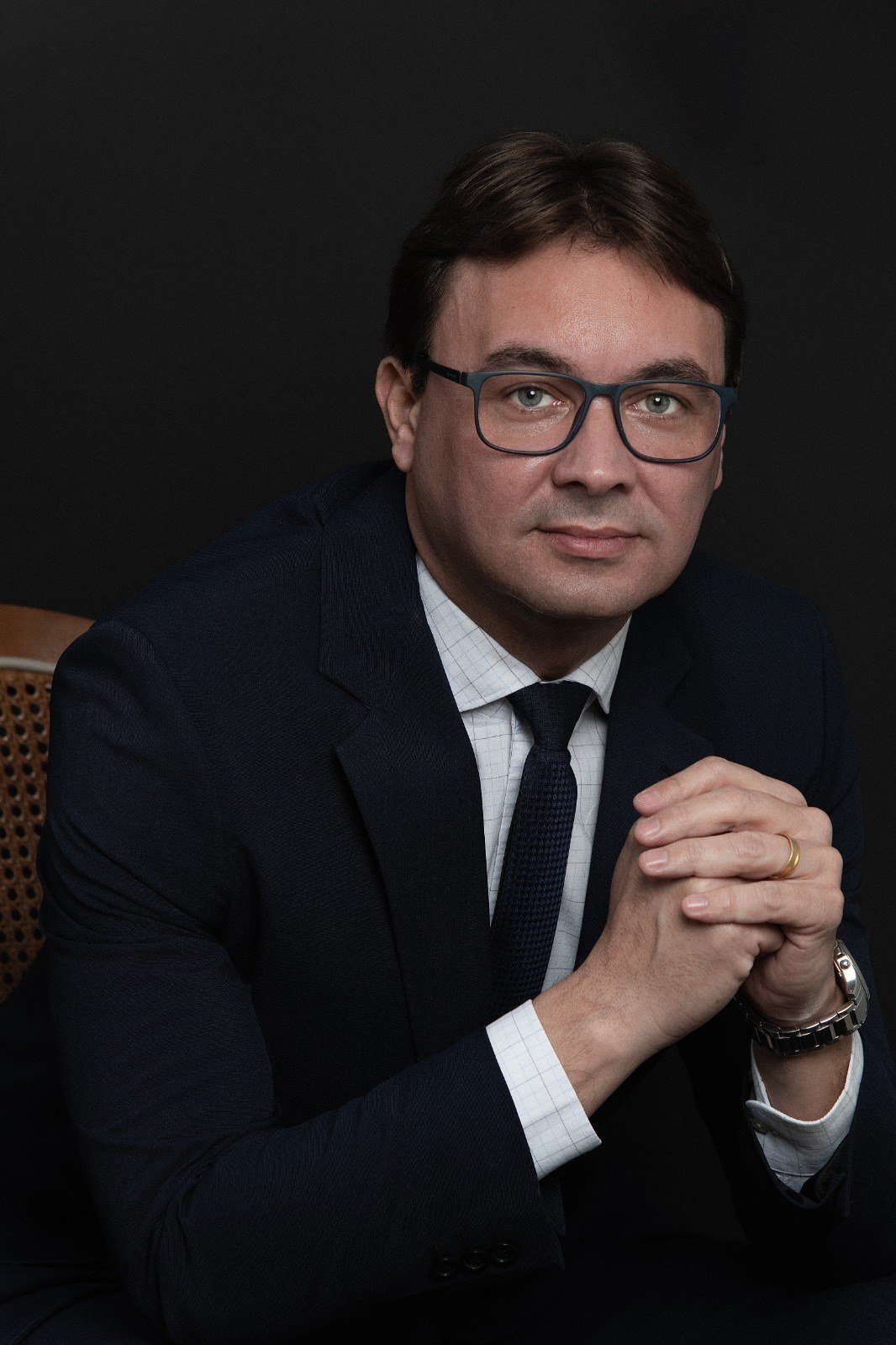 Marcel Lodetti Fábris, advogado, de terno escuro e óculos, com as mãos entrelaçadas, em retrato de estúdio